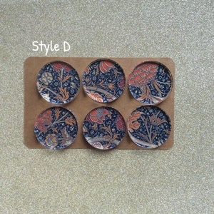 Puede incluir: Seis cabujones redondos de vidrio con un patr&oacute;n floral en tonos azules, naranjas y negros. Los cabujones est&aacute;n dispuestos en dos filas de tres sobre un fondo marr&oacute;n. El texto "Style D" est&aacute; impreso sobre los cabujones.