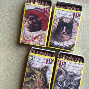 May include: Four vintage matchboxes with illustrations of cats. Each box has a different cat design and the number "119" printed on the front. The boxes are yellow with black trim.