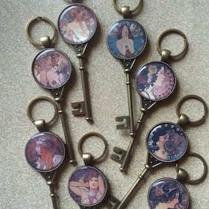 May include: A set of ten antique-style keychains with ornate metal key designs and round glass charms featuring Art Nouveau style illustrations of women.