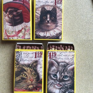 May include: Four matchboxes with yellow and white backgrounds feature vintage illustrations of cats. Each box has the number "119" printed on it. The cats are a black and white cat with a white collar, a brown tabby cat, a gray tabby cat, and a brown and white cat with a red hat.