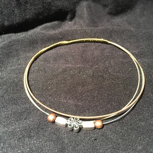 May include: A gold and copper wire bracelet with a silver flower charm.