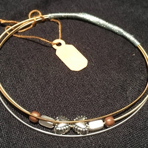 May include: Two gold and silver guitar strings are tied together to form a bracelet. The bracelet has brown and silver beads and two silver charms in the shape of hearts.