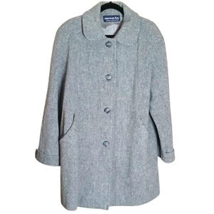 May include: A light gray wool coat with a rounded collar and three buttons down the front. The coat has two front pockets and the sleeves are cuffed. The label reads "Herman Kay".