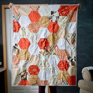 Peut inclure: Une courtepointe blanche et orange avec un motif hexagonal. La courtepointe est faite de différents tissus avec des motifs et des textures différents.