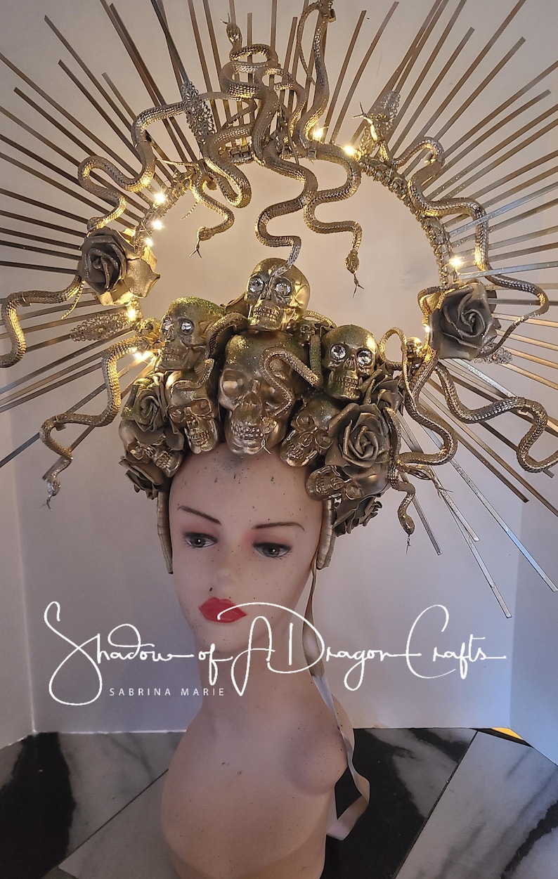 May include: A golden headpiece featuring skulls, roses, and snakes. The crown is adorned with decorative elements and lights, creating a dramatic effect. The headpiece is displayed on a mannequin head with red lipstick. The text "Shadow of A Dragon Crafts" is visible.