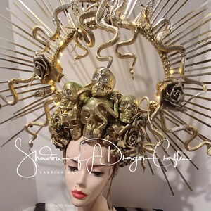 May include: A golden headpiece featuring multiple skulls, roses, and snakes. The headpiece has a halo design with radiating metal rods. The text "Shadow of A Dragon Crafts" is visible on the image.