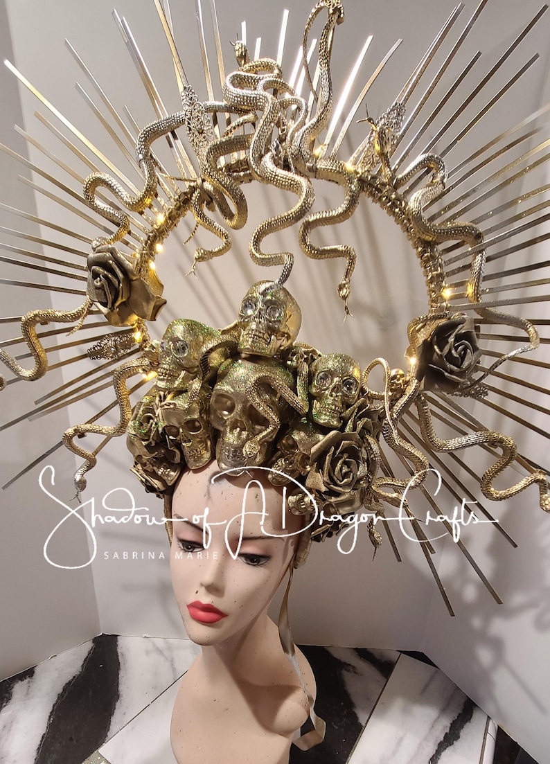 May include: A golden headpiece featuring multiple skulls, roses, and snakes. The headpiece has a halo design with radiating metal rods. The text "Shadow of A Dragon Crafts" is visible on the image.