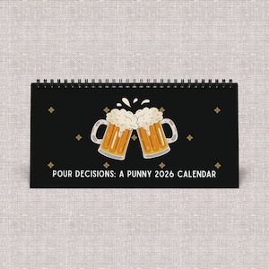 May include: A black desk calendar with a spiral binding. The cover features two cartoon beer mugs clinking together, with foam overflowing. The text "POUR DECISIONS: A PUNNY 2026 CALENDAR" is printed below the mugs.