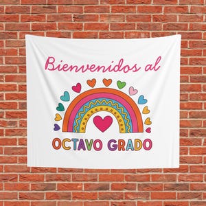 May include: A white wall tapestry featuring a colourful rainbow graphic with small hearts surrounding the arch. The text "Bienvenidos al" is printed in pink above the rainbow, and the text "OCTAVO GRADO" is printed in orange below it.