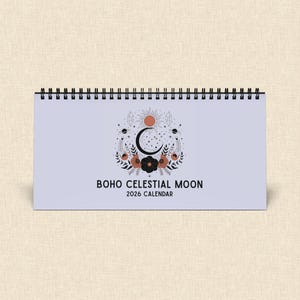Könnte beinhalten: Ein Spiral-Schreibtischkalender mit helllila Einband. Der Einband zeigt ein himmlisches Design mit einem Halbmond, einer Sonne, Sternen und floralen Elementen in Orange, Schwarz und Braun. Der Text "BOHO CELESTIAL MOON 2026 CALENDAR" ist darunter gedruckt.