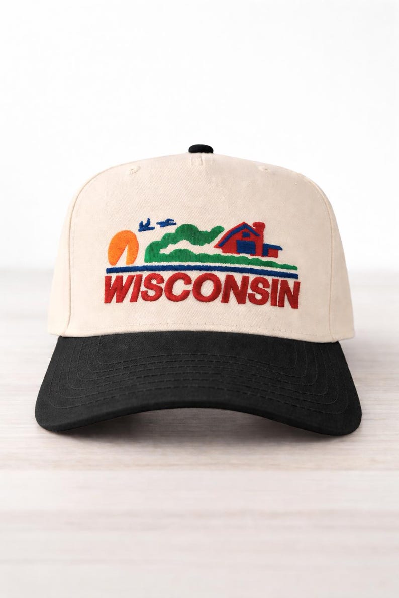 May include: Cream-colored baseball cap with a black brim. The cap features an embroidered design of a red house, green hills, a setting sun, and the word "WISCONSIN" in red and blue.
