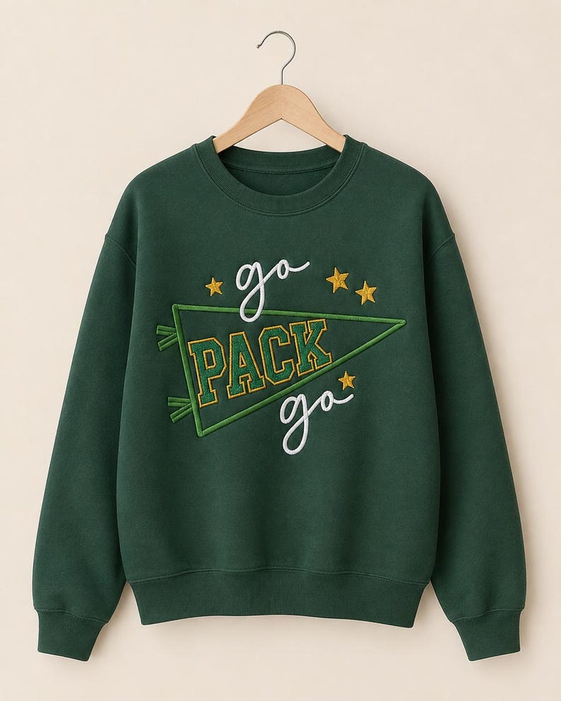 May include: A dark green crewneck sweatshirt featuring an embroidered design with the text "go PACK go" in white and yellow. The design includes a green pennant flag outline and three yellow embroidered stars on a long-sleeve pullover garment.