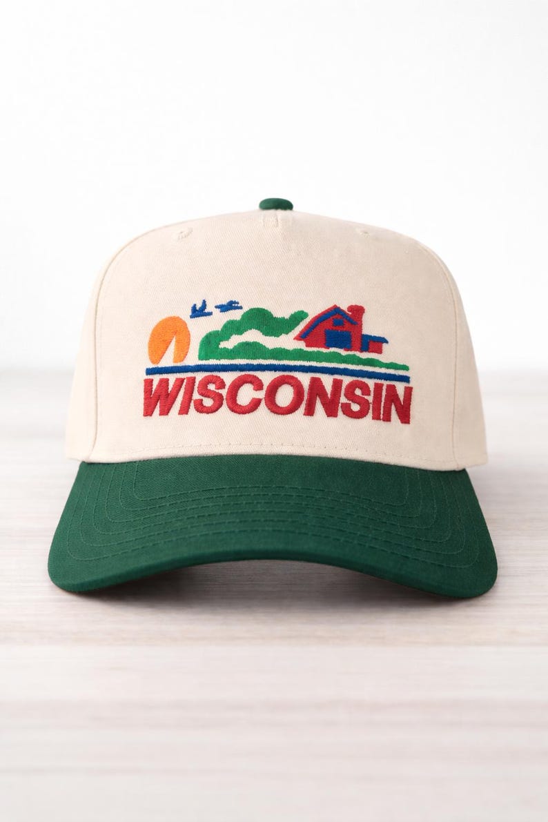 May include: Cream-colored baseball cap with a green brim. The cap features an embroidered design of a red house, green hills, an orange sun, and the word "WISCONSIN" in red letters.