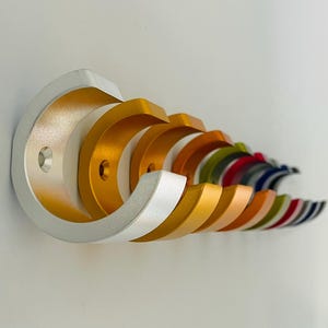 May include: A set of colourful metal hooks in various shades of gold, silver, green, red, blue and black. The hooks are arranged in a row, with the silver hook at the front and the black hook at the back.