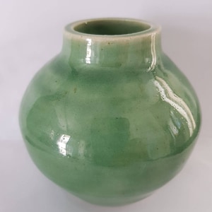 Könnte beinhalten: Eine kleine, runde, grüne Keramikvase mit glatter, glänzender Oberfläche.