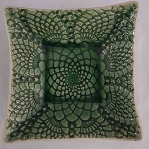 May include: A square ceramic dish with a green lace design. The dish has a raised rim and a smooth, glazed surface.