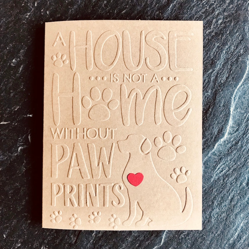 Puede incluir: Una tarjeta marr&oacute;n con el texto "Una casa no es un hogar sin huellas de patas" y una silueta de un perro con un coraz&oacute;n rojo en el pecho.