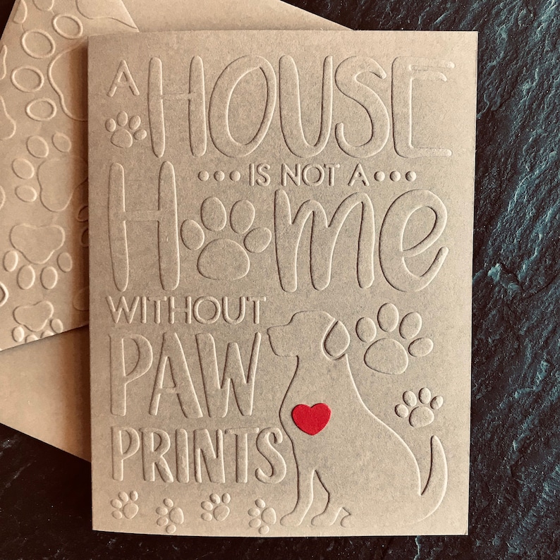 Puede incluir: Una tarjeta marr&oacute;n con el texto "Una casa no es un hogar sin huellas de patas" y una silueta de un perro con un coraz&oacute;n rojo en el pecho.