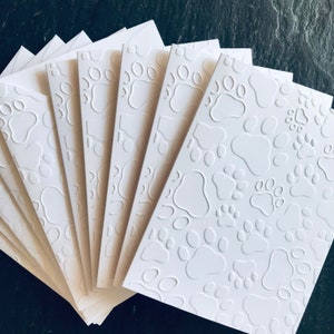 May include: A set of eight white blank cards with a raised paw print pattern. The cards are arranged in a fan shape.