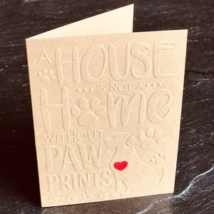 Puede incluir: Una tarjeta marr&oacute;n con el texto "Una casa... no es un... hogar sin huellas de patas" y un coraz&oacute;n rojo en el centro de una silueta de perro.