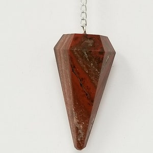 May include: A red jasper crystal pendulum with a silver chain. The pendulum is faceted and has a pointed tip.