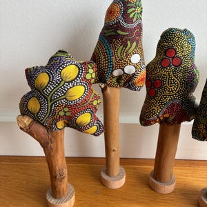 May include: Decorative fabric mushroom sculptures. The mushroom caps are made from patterned fabric in red, yellow, and blue. They have wooden stems and bases. The sculptures are artistic and handmade.