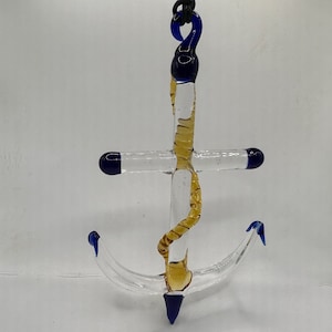 May include: A glass anchor pendant with a blue and gold rope design. The anchor is clear glass with blue accents and a gold rope design.