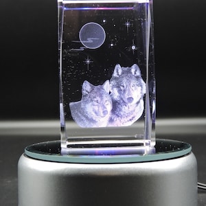 May include: A crystal cube with a 3D laser engraved image of two wolves howling at the moon. The cube is on a rotating base with a silver finish.