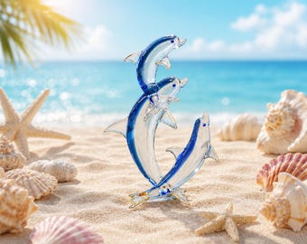 May include: A clear and blue glass sculpture featuring three dolphins leaping in an upward formation. The dolphins are crafted from translucent glass with deep blue accents along their fins and bodies, standing on a small, clear glass base.