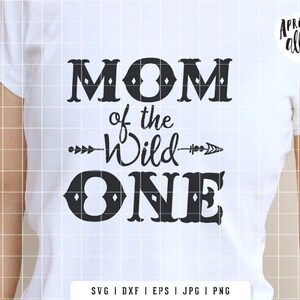 May include: White t-shirt with the text "MOM of the Wild ONE" in black. The design includes an arrow and decorative fonts. The brand name "Apricot Ally" is in the upper right corner.
