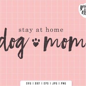 May include: Pink background with a grid pattern and the words "stay at home dog mom" in a dark gray script font. A paw print heart symbol is between "dog" and "mom". The Apricot Ally logo is in the upper right corner.