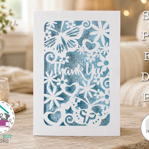 Könnte beinhalten: Eine weiße rechteckige Karte mit einem lasergeschnittenen Design aus Schmetterlingen, Blumen und Herzen, mit dem Text Thank You in der Mitte. Der Ausschnitt zeigt einen strukturierten blauen Hintergrund. Das Bild enthält den Text SVG, PNG, EPS, DXF, PDF.