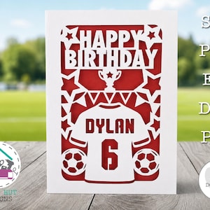 Może przedstawiać: Biała, warstwowa wycinanka z papieru na czerwonym tle z napisem HAPPY BIRTHDAY, trofeum, koszulką piłkarską z imieniem DYLAN i numerem 6, dwiema piłkami nożnymi oraz gwiazdkami. Projekt zawiera pliki SVG, PNG, EPS, DXF oraz PDF.