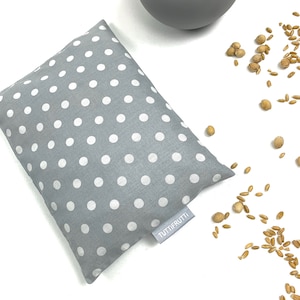 Puede incluir: Una bolsa de tela gris con lunares blancos y una etiqueta blanca que dice "Tuti Frutti!" La bolsa está llena de granos beige y está sobre una superficie blanca.