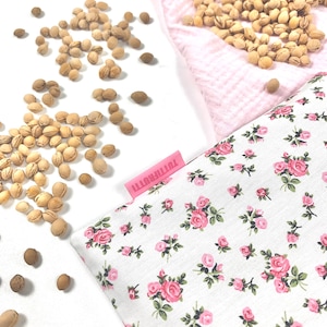 Könnte beinhalten: Ein weißer Stoffbeutel mit einem rosa Blumenmuster und einem rosa Etikett mit der Aufschrift "TUTTIFRUTTI" wird gezeigt. Um den Beutel herum sind hellbraune Samen und ein rosa, strukturiertes Gewebe verstreut.