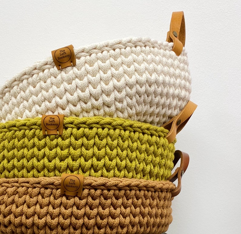 Pode incluir: Tr&ecirc;s cestas de croch&ecirc; empilhadas umas sobre as outras. A cesta de cima &eacute; branca, a cesta do meio &eacute; verde e a cesta de baixo &eacute; castanha. Cada cesta tem uma pega de couro castanho e uma etiqueta que diz "The Left Hookery".