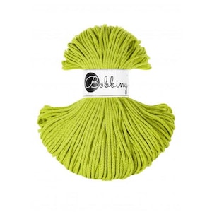 May include: A ball of bright green macrame cord with a white label that reads "Bobbiny" in a script font. The cord is tightly wound and has a soft, textured appearance, ideal for crafting projects.