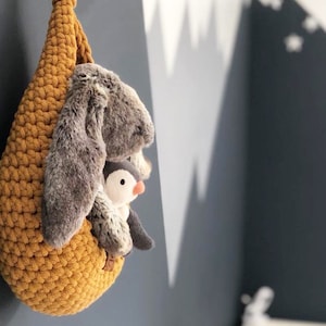 May include: A mustard yellow crocheted hanging basket with a gray bunny and a penguin stuffed animal inside.