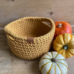 May include: A yellow crocheted basket with a leather tag that says "The Left Bankery". The basket is surrounded by three small pumpkins.