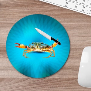 May include: A blue and white mouse mat with a crab and a knife on it. The crab is facing the viewer and the knife is sticking into the crab's back.