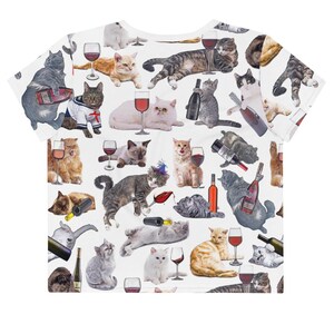 May include: White crop top with a repeating pattern of cats drinking wine. The cats are in various poses and have different colored fur. The wine glasses are filled with red wine.