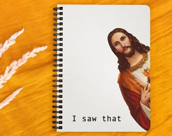 Puede incluir: Un cuaderno blanco de espiral con encuadernación negra. La portada presenta una imagen impresa de Jesucristo asomándose desde el lado derecho de la página. El texto "I saw that" está impreso en negro en la parte inferior de la página.