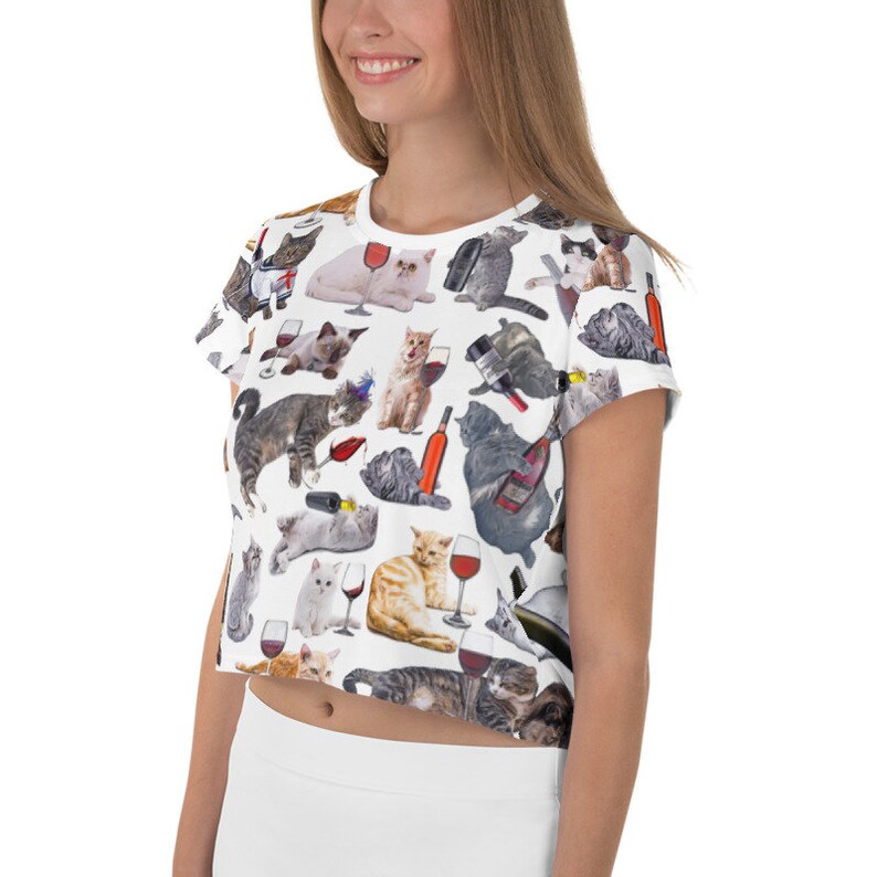 May include: White crop top with a print of cats drinking wine. The cats are in various poses and are wearing different accessories. The print is all over the shirt.