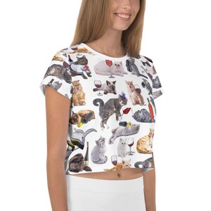 May include: White crop top with a repeating pattern of cats drinking wine. The cats are in various poses and wearing different accessories, such as hats and glasses.