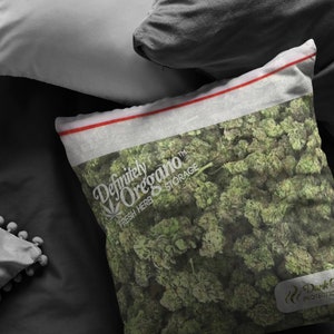 Peut inclure: Un oreiller blanc avec une fermeture &eacute;clair rouge et le texte "Definitely Oregano&trade; Fresh Herb Storage" imprim&eacute; dessus. L'oreiller est rempli d'origan vert s&eacute;ch&eacute;.