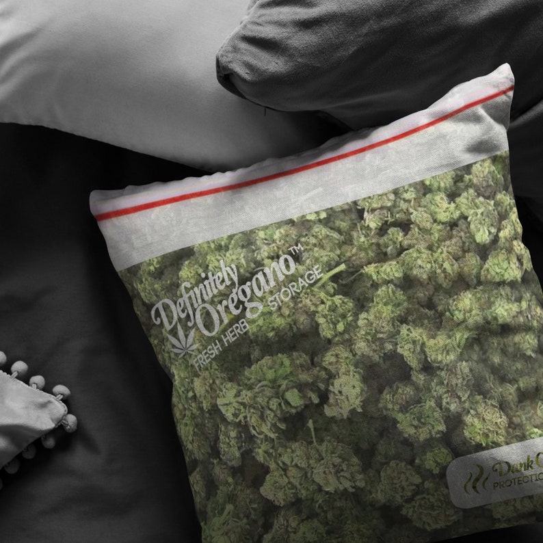 Peut inclure: Un oreiller blanc avec une fermeture &eacute;clair rouge et le texte "Definitely Oregano&trade; Fresh Herb Storage" imprim&eacute; dessus. L'oreiller est rempli d'origan vert s&eacute;ch&eacute;.