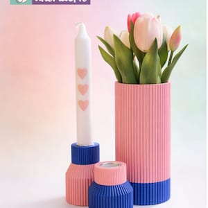 May include: A still life arrangement with a white candle adorned with pink hearts, a pink and blue vase holding tulips, and two matching candle holders. The items are in shades of pink and blue, with a ribbed texture. The logo "unikatHi" is in the upper left corner.