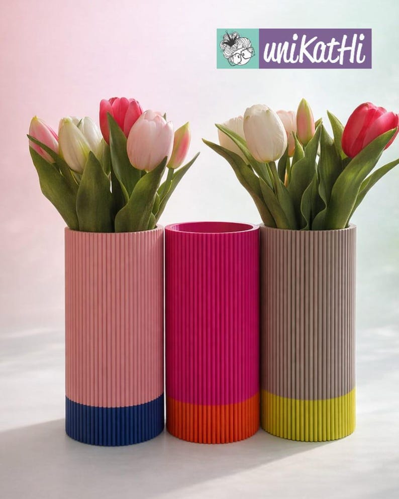 May include: Three cylindrical vases with vertical ribbed texture, each holding tulips. The vases are pink, fuchsia, and taupe, with contrasting coloured bases in blue, orange, and yellow. The top right corner has the text "uniKatHi".