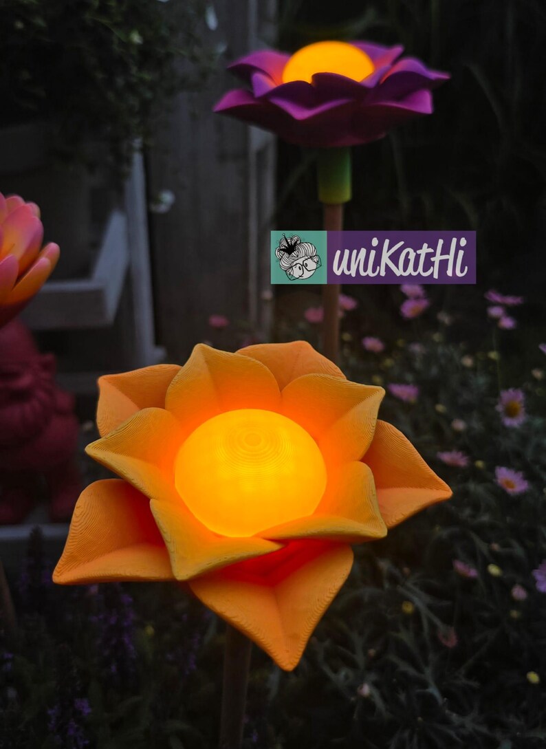 Puede incluir: Luces solares con forma de flor naranja y morada con centros brillantes. Los p&eacute;talos de las flores son detallados y las luces est&aacute;n sobre estacas de madera. Incluye el texto "uniKatHi".