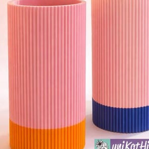 May include: Two cylindrical planters with vertical ribbed texture. One is pink with an orange base, the other is pink with a blue base. The planters are empty and ready for plants. The planters are a modern home decor item.
